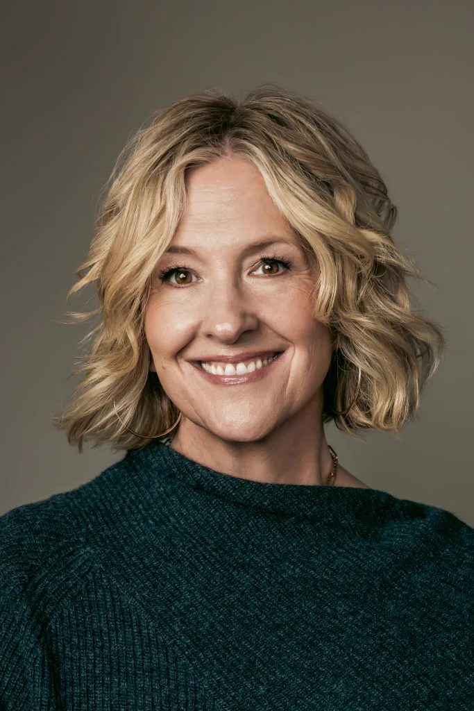 A person with curly hair smiling and wearing a blue shirt.